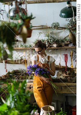 Surprised florist woman surrounded by collection of tillandsia air plants, charmed with pleasant gift, looking at a bouquet of irises flowers. Indoor garden Surprised florist woman surrounded by collection of tillandsia air plants, charmed with pleasant gift, looking at a bouquet of irises flowers. Indoor garden 136174312