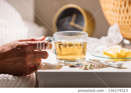 Sick man in bed holding cup of hot tea with lemon, drinking hot beverage to get well from flu Sick man in bed holding cup of hot tea with lemon, drinking hot beverage to get well from flu 136174323