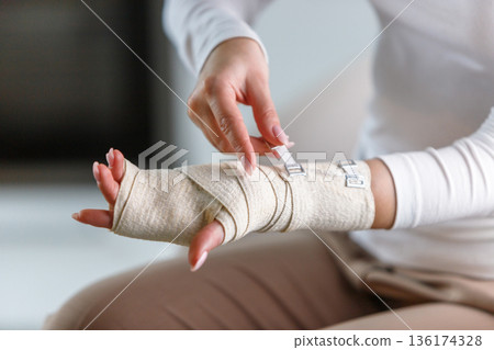 woman wrapping her painful wrist with elastic orthopedic bandage woman wrapping her painful wrist with elastic orthopedic bandage 136174328