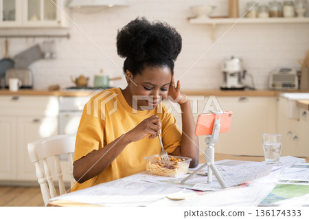 Young african female calling friends online via video chat in home kitchen at lunch break from study 136174333