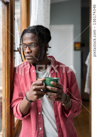 Depressed sad African guy holding cup of tea looking out window, having problems in personal life Depressed sad African guy holding cup of tea looking out window, having problems in personal life 136174346