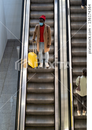Black man stands on escalator in airport wear face mask to protect from contact with Nipah virus Black man stands on escalator in airport wear face mask to protect from contact with Nipah virus 136174364