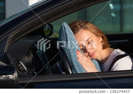 Tired young woman driver asleep on pillow on steering wheel, resting after long hours driving a car. Fatigue 136174457