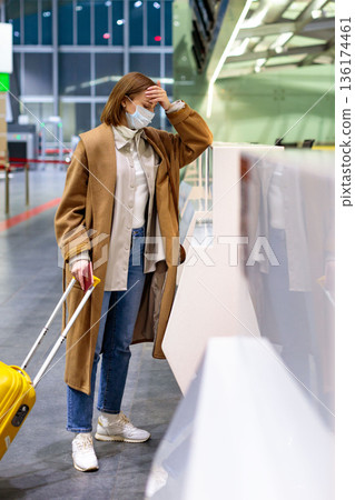 Woman with luggage upset over flight cancellation, stands at check-in counters at airport terminal 136174461