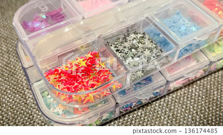 Close-up of colorful star-shaped sequins and glitter in a plastic organizer box for DIY craft projects. Close-up of colorful star-shaped sequins and glitter in a plastic organizer box for DIY craft projects. 136174485