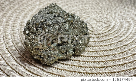 Raw pyrite crystal cluster with metallic shine on a neutral braided background for geology projects. Raw pyrite crystal cluster with metallic shine on a neutral braided background for geology projects. 136174494