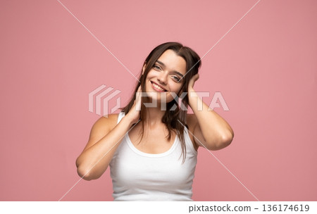 Young brunette woman with natural makeup and calm expression posing against pink background in clean minimalist studio portrait Young brunette woman with natural makeup and calm expression posing against pink background in clean minimalist studio portrait 136174619