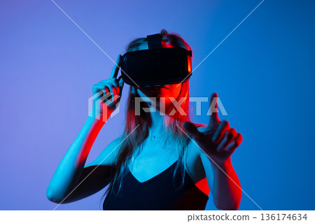 Young woman playing VR game using virtual reality headset and hand gestures in futuristic neon light studio environment 136174634