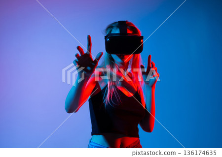 Woman using VR headset and reaching forward with hands, immersive virtual reality experience with futuristic neon lighting 136174635
