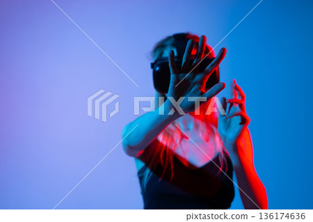 Woman Reaching Toward Virtual Interface in VR Headset, Futuristic Technology Concept With Neon Red and Blue Lighting 136174636