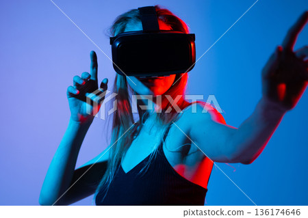 Woman pointing at virtual interface while wearing VR headset, immersive gesture control and futuristic technology 136174646