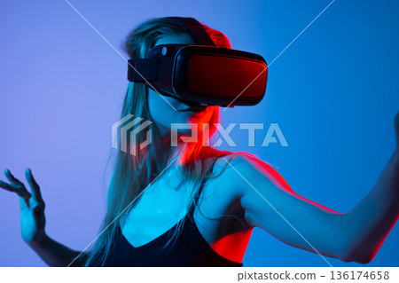 Woman interacting in virtual space with VR headset and extended arm, immersive metaverse technology concept 136174658