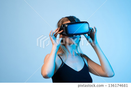 Woman using virtual reality headset in studio with blue light, immersive technology and futuristic digital interaction 136174681