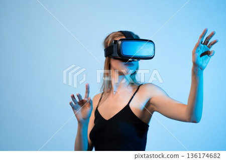Female user interacting with virtual environment using hand gestures in VR headset, immersive digital technology concept 136174682