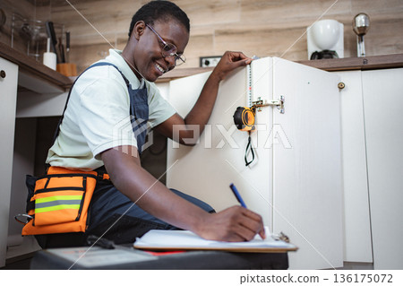 Female Carpenter Taking Measurements of Kitchen Cabinets and Writing Notes Female Carpenter Taking Measurements of Kitchen Cabinets and Writing Notes 136175072