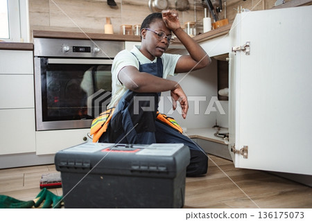 Tired plumber taking a break during kitchen sink repair 136175073