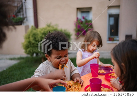 Diverse children enjoying spaghetti dinner together outdoors 136175080