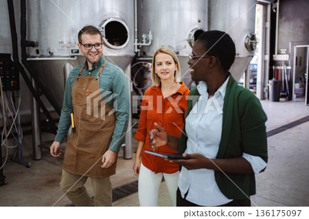 Brewery owner leading tour for diverse visitors in industrial setting 136175097