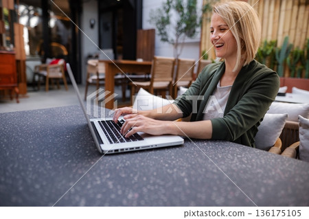 Blonde woman working on laptop computer smiling outdoors cafe Blonde woman working on laptop computer smiling outdoors cafe 136175105