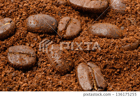 Whole roasted coffee beans lie on an even layer of freshly ground brown coffee. 136175255