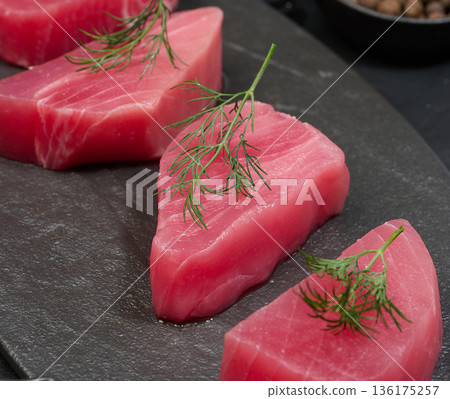 Raw piece of tuna with a sprig of dill on a black board 136175257