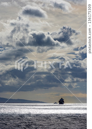 Dark storm clouds over open sea with distant small boat creating moody maritime atmosphere. 136175309