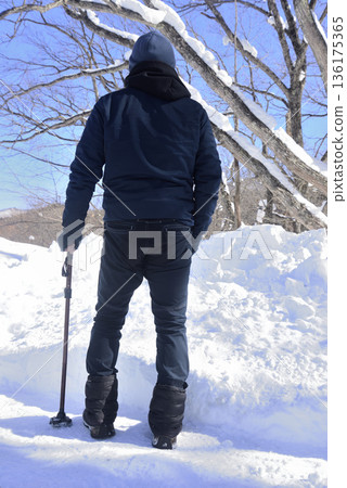 An elderly man doing rehabilitation using a walking stick on a snowy road 136175365
