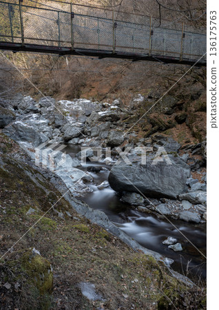 The source of the Arakawa River in Chichibu in winter, with a clear stream flowing through a frozen valley and a suspension bridge on a hiking trail 136175763