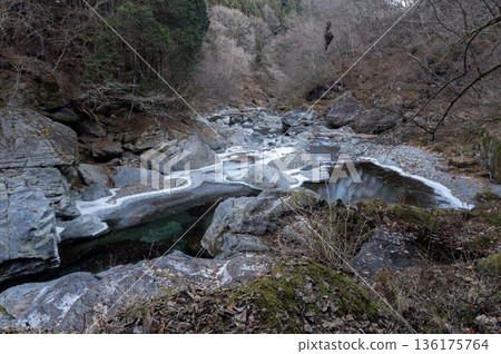 The source of the Arakawa River in Chichibu in winter, with the clear stream flowing through the frozen valley and huge rocks 136175764