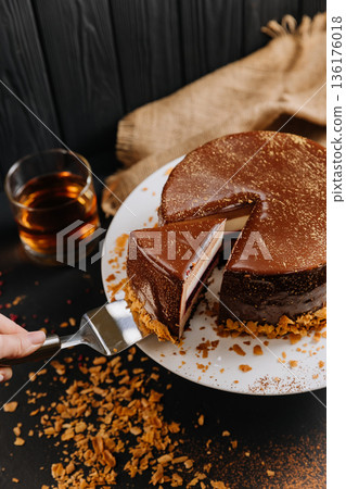 Layered chocolate mousse cake slice with raspberry jelly on spatula, dark background 136176018