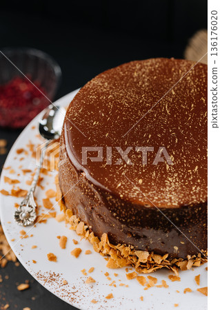 Close up glossy chocolate cake with crumbs and cocoa on white plate, dark background Close up glossy chocolate cake with crumbs and cocoa on white plate, dark background 136176020
