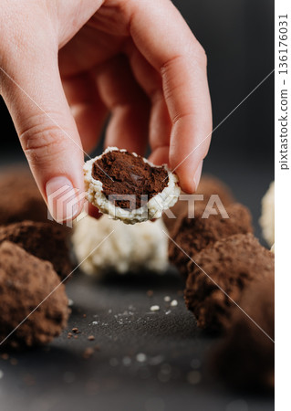 Hand holding cut coconut truffle with dark chocolate filling, macro on black Hand holding cut coconut truffle with dark chocolate filling, macro on black 136176031