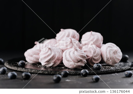Pink meringues with blueberries on slate plate, dark background, sugar dust 136176044