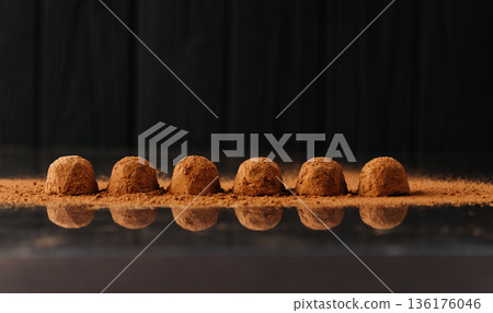 Cocoa dusted chocolate truffles in a row with reflection on black background 136176046