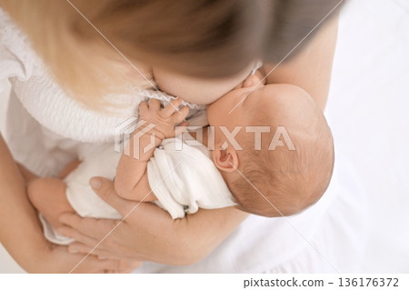 Mother gently breastfeeding newborn baby at home. Concept of motherhood, natural feeding, infant nutrition, bonding, care, and early childhood. Mother gently breastfeeding newborn baby at home. Concept of motherhood, natural feeding, infant nutrition, bonding, care, and early childhood. 136176372
