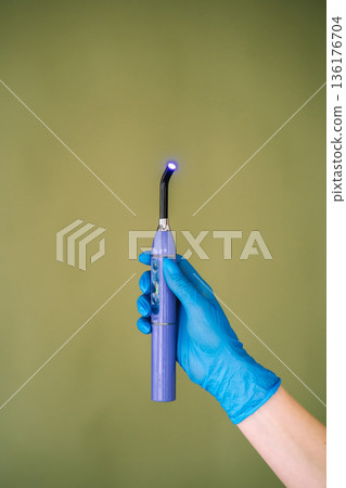Dental curing light in gloved hand on green background Dental curing light in gloved hand on green background 136176704