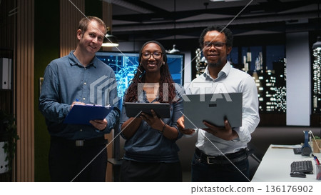 Portrait of smiling tech startup colleagues brainstorming ways to optimize performance in office. Happy programmers use devices for debugging, typing lines of code 136176902