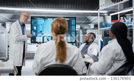 Senior scientist presenting new drug development findings to pharmaceutical team in lab. Expert pointing at large screen displaying cellular reaction during training meeting, camera B 136176903