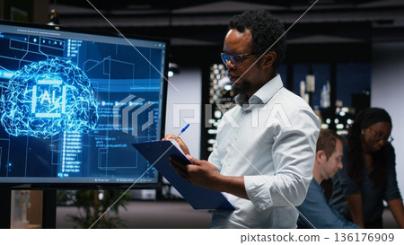 Manager in office writing on notepad, taking notes of artificial intelligence system bugs to fix. Supervisor looking at large screen, documenting neural network errors during troubleshooting Manager in office writing on notepad, taking notes of artificial intelligence system bugs to fix. Supervisor looking at large screen, documenting neural network errors during troubleshooting 136176909