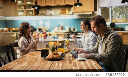 Busy working dad typing on laptop at kitchen table with his family, ignoring his pre-teen girl and wife during breakfast. Distracted preoccupied father distant with his daughter. 136176912