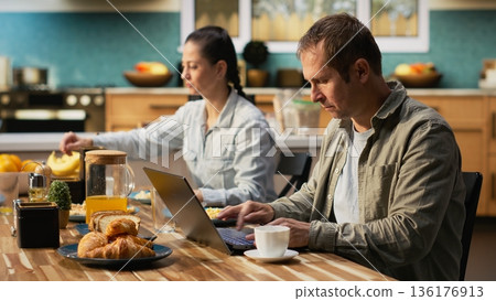 Busy working dad typing on laptop at kitchen table with his family, ignoring his pre-teen girl and wife during breakfast. Distracted preoccupied father distant with his daughter. 136176913