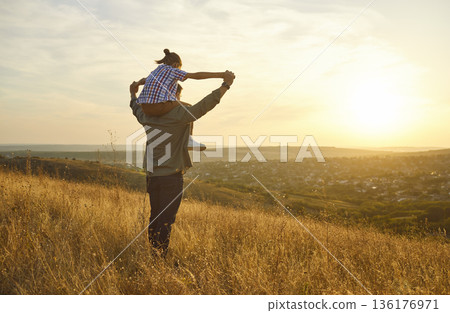 Happy father and child at sunset, shoulders ride across scenic hill meadow Happy father and child at sunset, shoulders ride across scenic hill meadow 136176971