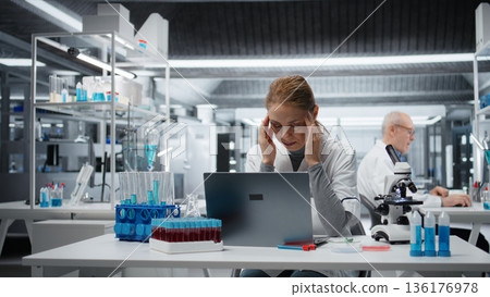 Tired female scientist feeling headache while working on laptop in lab, studying genomics. Exhausted researcher feeling pain while studying DNA strand mapping on notebook, camera A Tired female scientist feeling headache while working on laptop in lab, studying genomics. Exhausted researcher feeling pain while studying DNA strand mapping on notebook, camera A 136176978