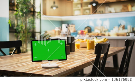 Chroma key display on tablet placed on dining table in rustic empty kitchen, cozy space filled with utensils, cooking essentials, kitchenware and stylish luxury appliances. 136176998
