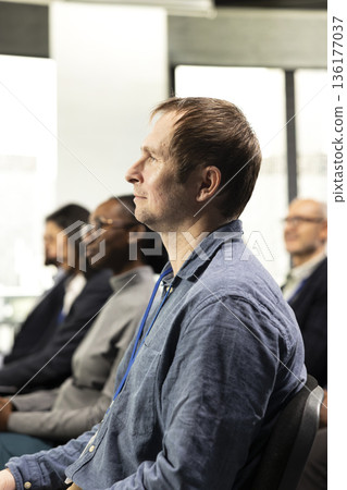 Male CEO attends professional business event in conference room with panel presentation. Listening to speaker promoting leadership and entrepreneurship values among participants. 136177037