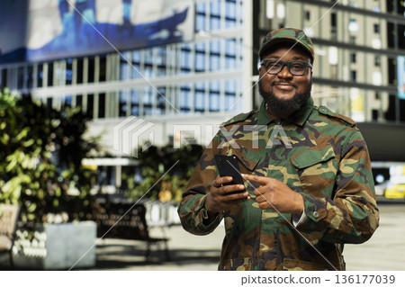 African american service person in full gear opens mobile phone map, walking through a modern downtown area in uniform. Soldier admiring skyscrapers and busy city street life. African american service person in full gear opens mobile phone map, walking through a modern downtown area in uniform. Soldier admiring skyscrapers and busy city street life. 136177039