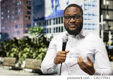 Adult male correspondent conducts outdoor interview on a city street, using confident voice and on air communication to share press coverage and important public information downtown. Adult male correspondent conducts outdoor interview on a city street, using confident voice and on air communication to share press coverage and important public information downtown. 136177041