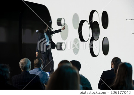 Asian senior designer introducing new mobile phone announcement with visuals on stage for promotion, advertising new release for investment deal during convention. Launch event. Asian senior designer introducing new mobile phone announcement with visuals on stage for promotion, advertising new release for investment deal during convention. Launch event. 136177043