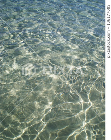 The stunning, glass-clear surface of the Stintino sea near Olbia, Sardinia, Italy, reflects vibrant turquoise and light blue tones under the Mediterranean sun. Calm, shallow waters reveal exceptional 136177085