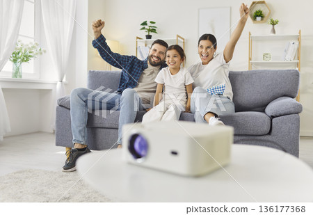 Happy family watching movie, sports match or TV show with projector at home Happy family watching movie, sports match or TV show with projector at home 136177368